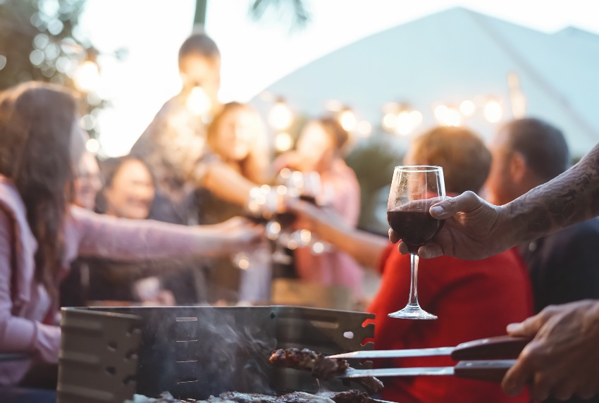 Zu hellem Fleisch, welches moderat gewürzt ist, bietet sich ein etwas zurückhaltender Rotwein an Fröhliche Familie beim feierlichen Toast auf der Grillparty - Junge und ältere Eltern haben Spaß beim gemeinsamen Essen im Garten - Dinner-BBQ-Essen und Jugendaktivitäten für ältere Menschen