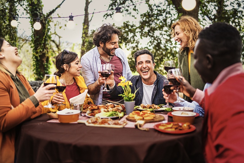 Zu vielen Grillklassikern kann man ohne Zögern zu einen klassischen italienischen Rotwein greifen Gesellschaft von fröhlichen Menschen, die am Grilltisch plaudern und sich zusammen entspannen, gegrilltes Essen essen und Wein trinken - Zeitvertreib der besten Freunde beim Bauernbankett - Lifestyle-Konzept für multiethnische Menschen - Wein zum Grillen